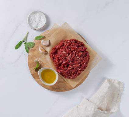 Ground Venison placed on board with garlic cloves, basil leaves, salt and cooking oil