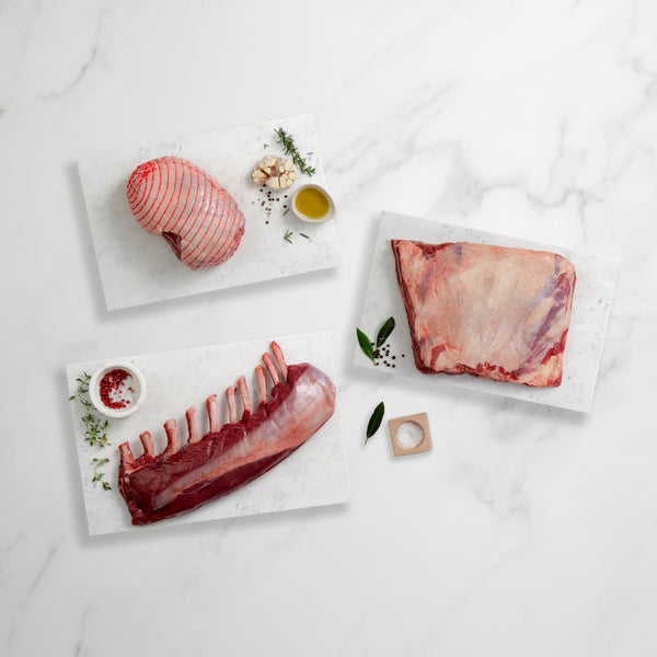 Three pieces of raw meat on marble slabs with herbs and spices on a light gray background