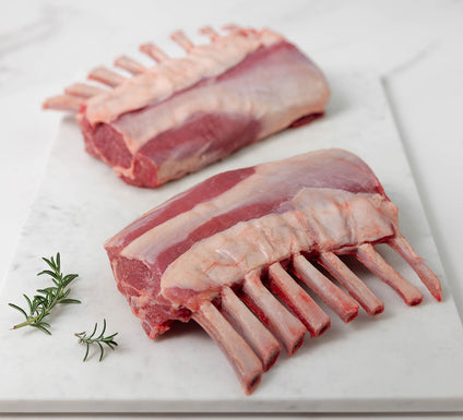 Two raw lamb racks on a white marble surface with fresh rosemary sprigs.