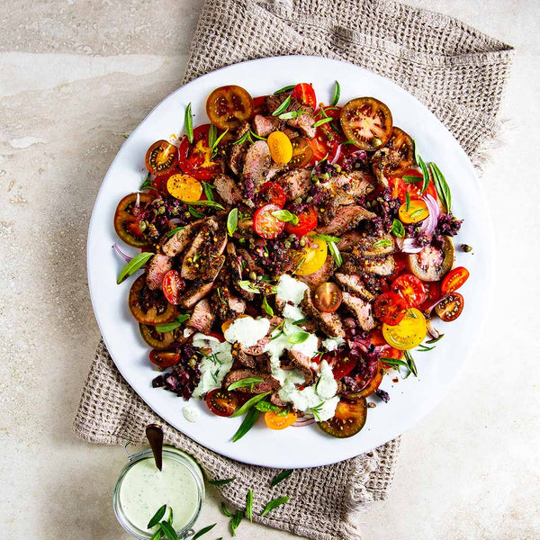 Plated dish of salad with tomatoes and lamb loin meat on a light background