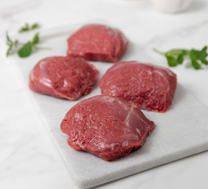 Raw lamb rumps on a white marble cutting board with fresh herbs.