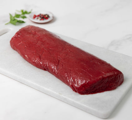 raw venison short loin meat on a white marble cutting board with spices and herbs at the background
