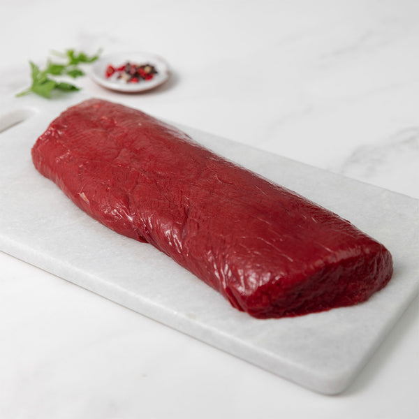 raw venison short loin meat on a white marble cutting board with spices and herbs at the background