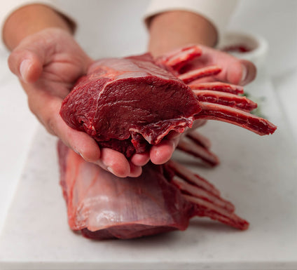 Raw venison rack meat being held in a person's hand on a white surface