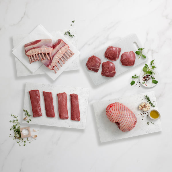 Assorted raw meats on marble slabs with herbs and spices on a light background