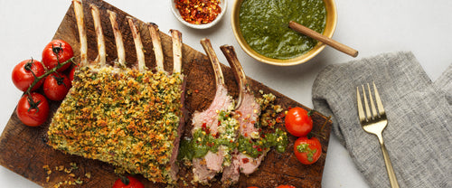 Herb-crusted lamb rack sliced and served on a wooden board with salsa verde and roasted cherry tomatoes, styled with rustic cutlery and garnishes—perfect for showcasing a premium lamb recipe.