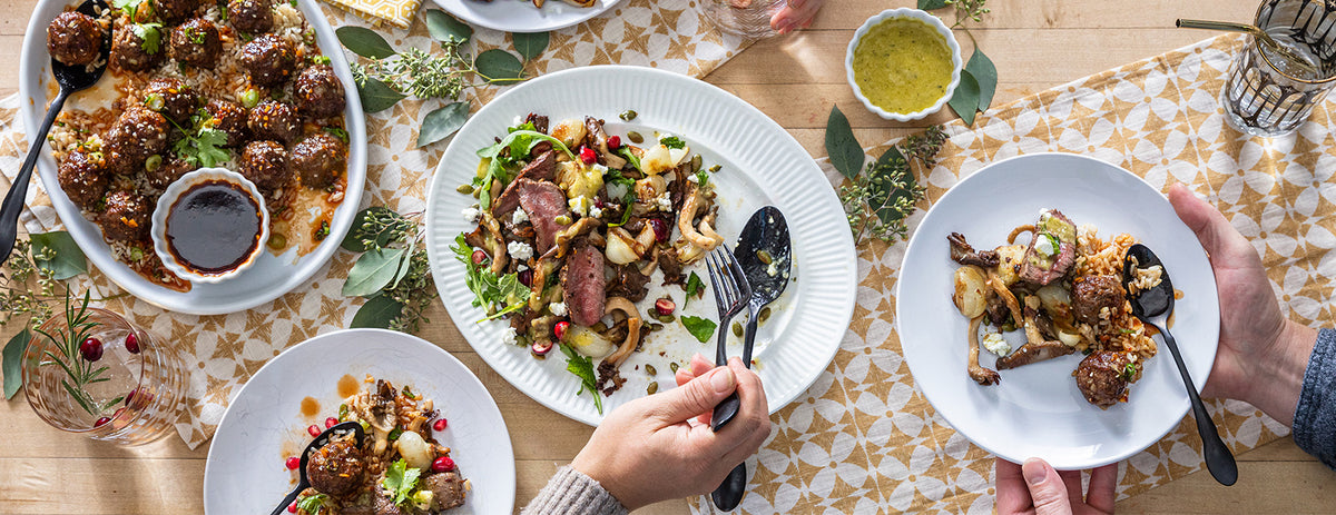 Dinner table with plates of food, cutlery, and drinks on a patterned tablecloth.