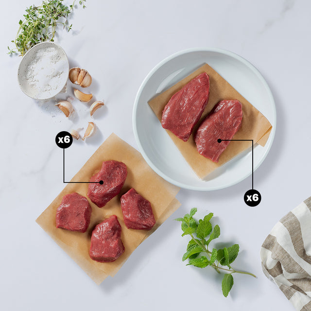 4 Pieces of lamb medallions with x6 blurb and 2 pieces of lamb steaks with x6 blurb placed with garlic cloves, herbs, and salt at the side