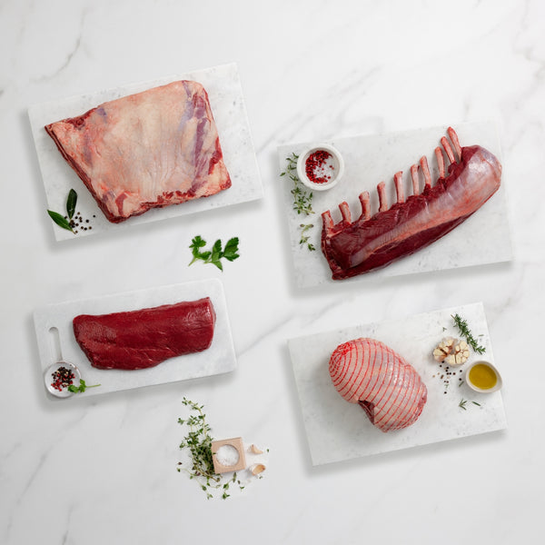 Assorted raw meat on marble slabs with herbs and spices on a light background
