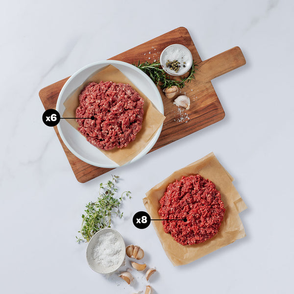 Ground meat on plates with herbs and spices on a wooden cutting board.