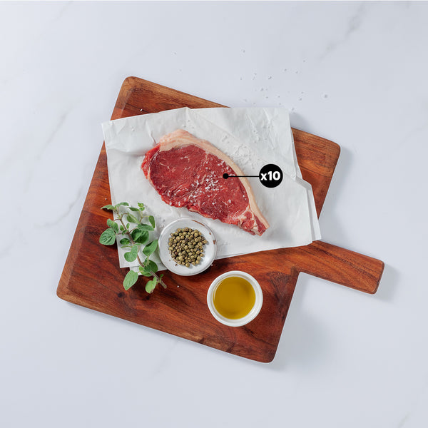 10oz New York Strip Beef steak sprinkled with salt placed on board showing x10 blurb with herbs, pepper and salt in bowl