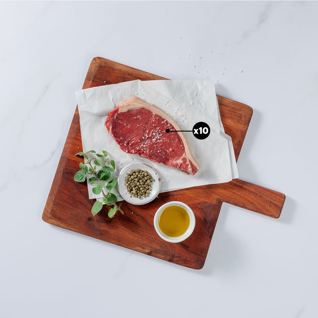 10oz New York Strip Beef steak sprinkled with salt placed on board showing x10 blurb with herbs, pepper and salt in bowl