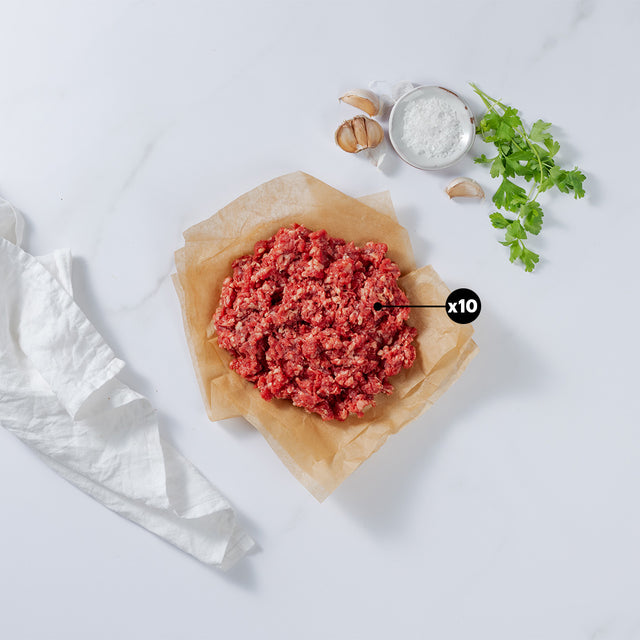 1 lb of Ground Beef placed on baking paper showing x10 blurb with garlic cloves, herbs, salt and kitchen towel at the side