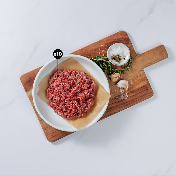 1 lb of Ground Lamb placed on baking paper in a bowl showing x10 blurb with garlic cloves, rosemary, salt and pepper on a board