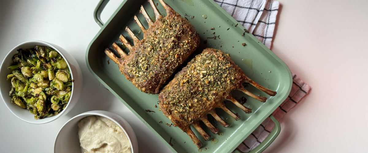 Rack of lamb on a green tray with side dishes on a light surface