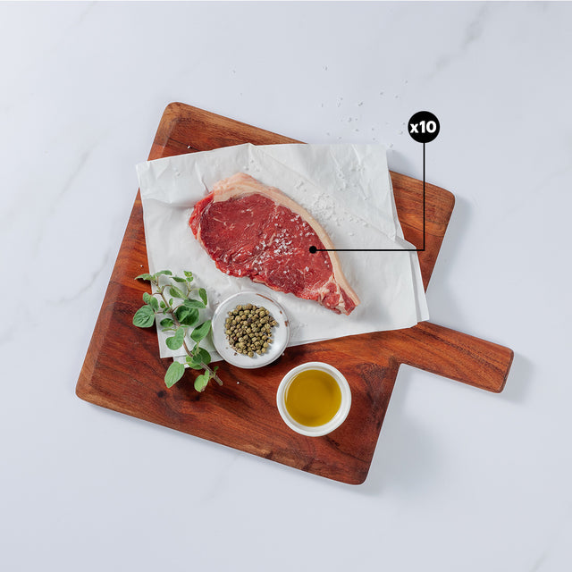 10oz New York Strip Beef steak sprinkled with salt placed on board showing x10 blurb with herbs, pepper and salt in bowl