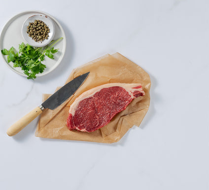 Silver Fern Farms Beef New York Strip Steak placed on paper with knife, coriander and peppers on the side