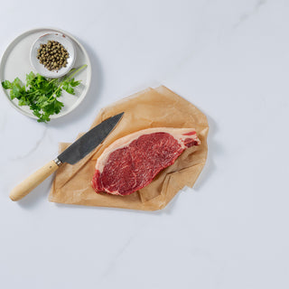 Silver Fern Farms Beef New York Strip Steak placed on paper with knife, coriander and peppers on the side