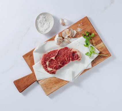 Silver Fern Farms Beef Rib Eye Steak placed on board with garlic cloves, salt and coriander