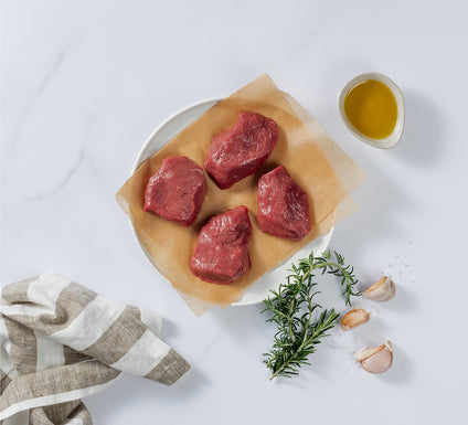 4 Pieces of Silver Fern Farms Lamb Medallion placed on plate with rosemary, garlic cloves, and olive oil at the side