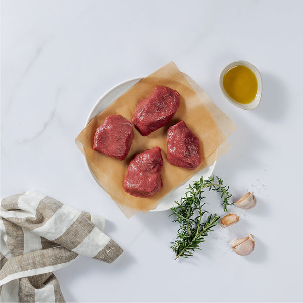 4 Pieces of Silver Fern Farms Lamb Medallion placed on plate with rosemary, garlic cloves, and olive oil at the side