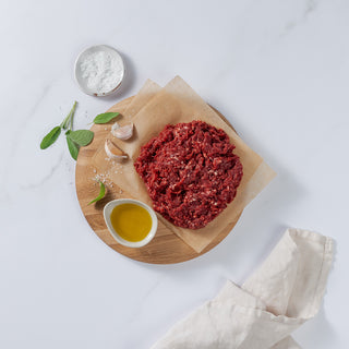 Ground Venison placed on board with garlic cloves, basil leaves, salt and cooking oil