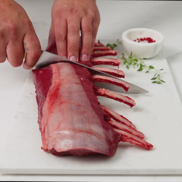 A person slicing a venison rack into two halves, each with five ribs, and then lifting it to display both the top and underside.