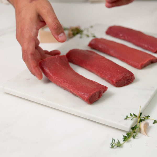 Placing four raw boneless lamb loins on a marble board and sprinkling salt over them.