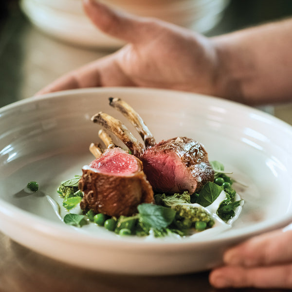 Lamb dish with green peas and herbs on a white plate, held by hands.