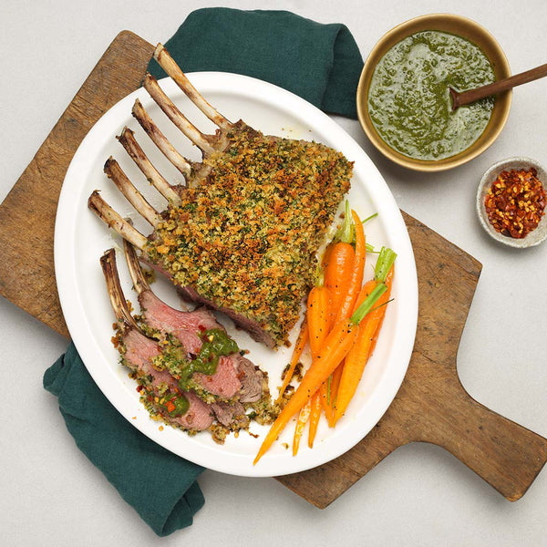 Lamb rack with vegetables on a white plate, served on a wooden cutting board.
