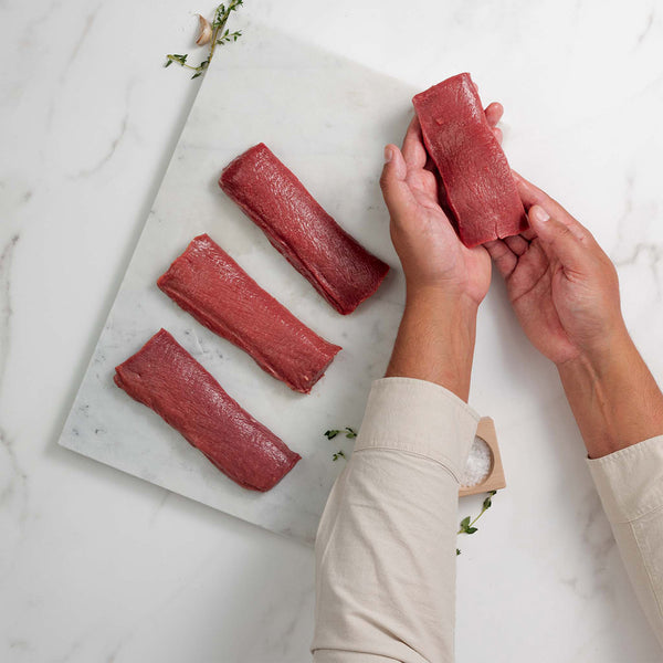 Person holding a piece of raw lamb loin fillet meat on a marble surface