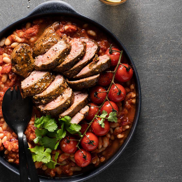 Sliced lamb rumps with beans and tomatoes in a black bowl.
