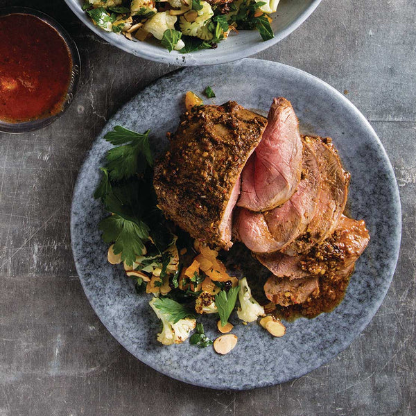 Sliced roasted lamb rump with vegetables on a gray plate.