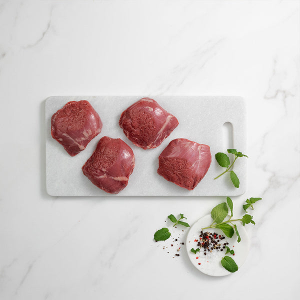 Four raw lamb rumps on a marble cutting board with herbs and spices.