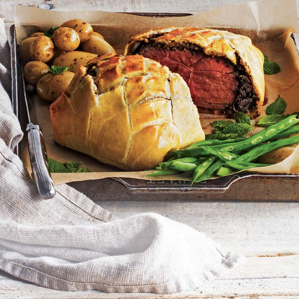 lamb rumps wellington dish cut to half with potatoes and vegetables on a tray