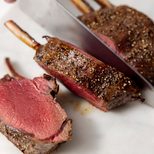 Sliced rack of venison with a knife on a white marble board