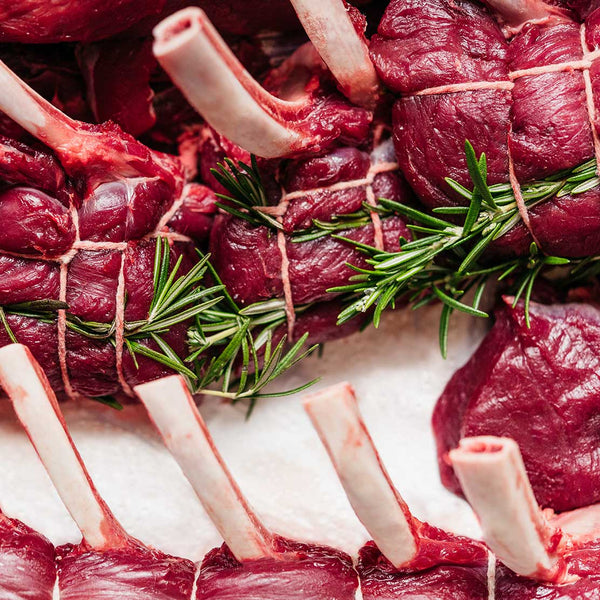 Raw venison racks with rosemary on a white surface