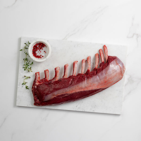Raw venison rack on a marble slab with spices on a light background