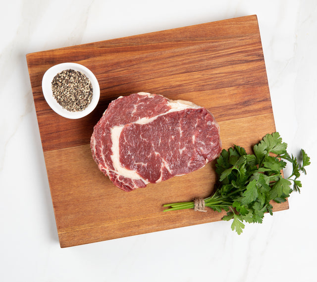 Silver Fern Farms Net Carbon Zero Beef Raw Rib-Eye Steak on board with ground pepper and cilantro at the side